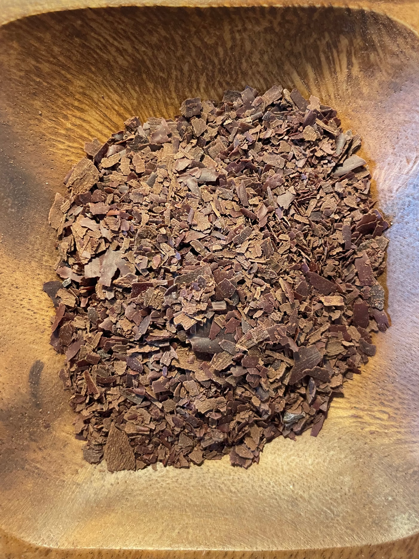 Geraspelte Kakaomasse in einer Holzschale, Nahaufnahme von oben.