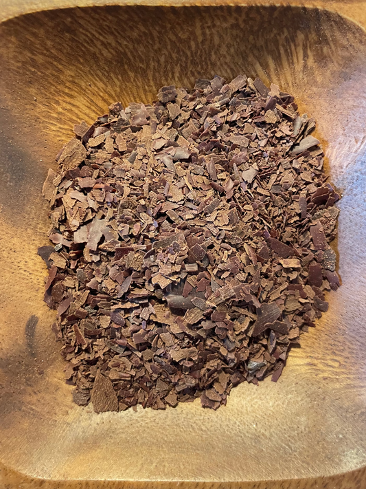 Geraspelte Kakaomasse in einer Holzschale, Nahaufnahme von oben.