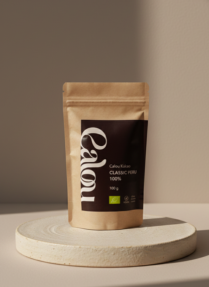 100 g Packung ‚Calou Kakao Pure Peru 100%‘ in brauner Kraftpapierverpackung mit schwarzem Etikett, stehend auf heller Oberfläche vor hellem Hintergrund.