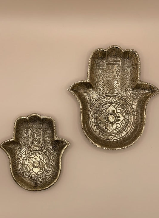 Zwei unterschiedlich große ornamentierte Messing-Schalen in Handform, nebeneinander vor warm beigefarbenem Hintergrund.