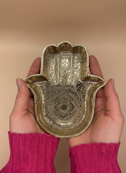 Ornamentierte Messing-Schale in Handform, gehalten mit beiden Händen vor warm beigefarbenem Hintergrund.